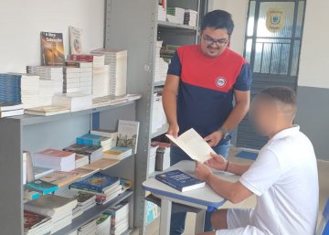 Na fotografia aparecem dois homens, um de pé e outro sentado lendo um livro