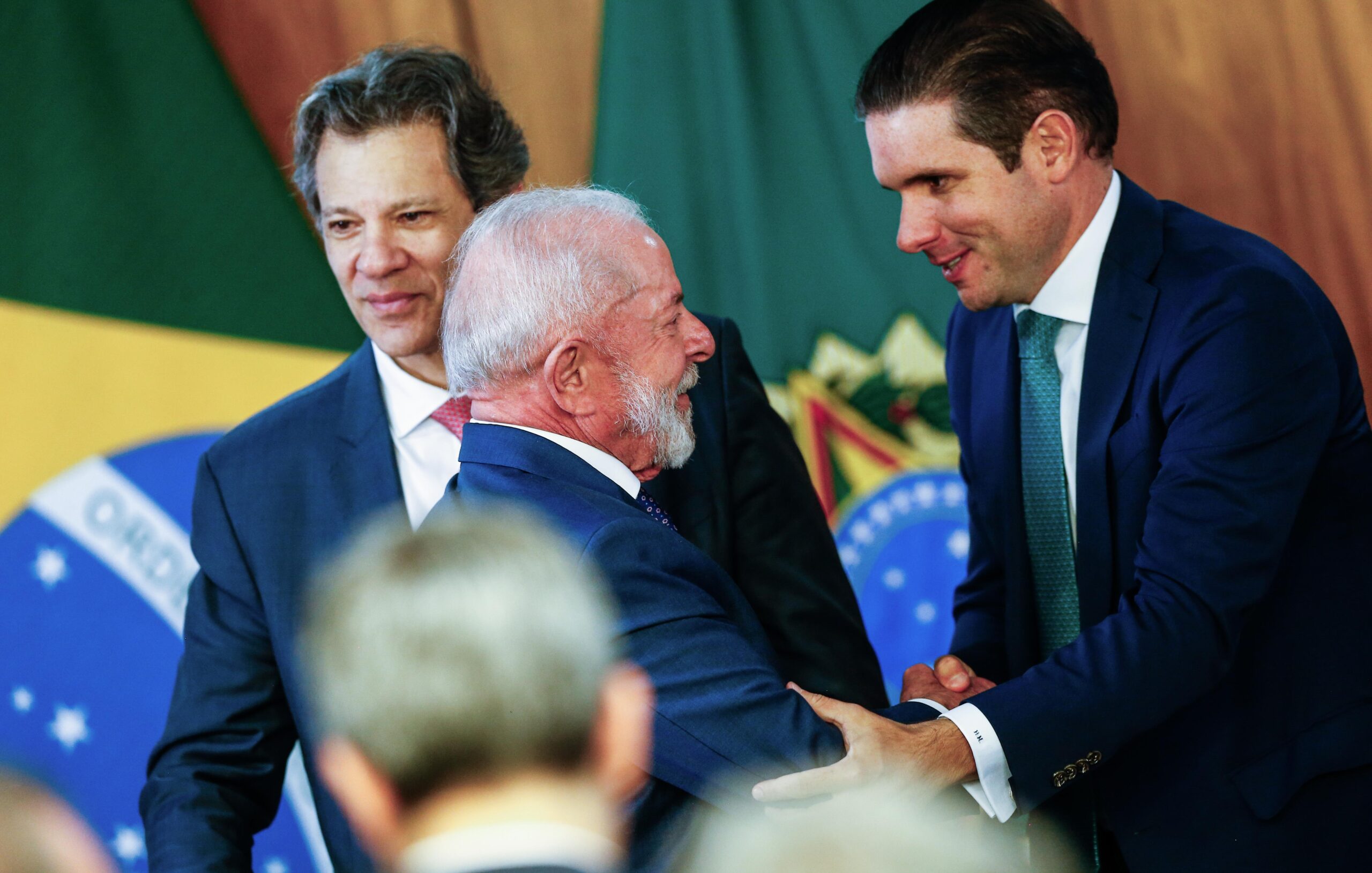 Hugo Motta cumprimenta o presidente Lula diante do ministro Fernando Haddad no dia 13 de agosto, no lançamento do plano Brasil Soberano.