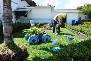 Na fotografia temos um reeducando de blusa clara, calça jeans e chapeu amarelo trabalhando no jardim do presídio